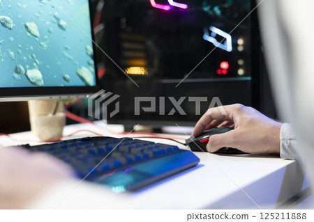 Person in neon lit apartment playing singleplayer videogame with spaceship shooting laser bullets at asteroids. Close up of gamer using crosshair overlay to hit targets in science fiction arcade game Person in neon lit apartment playing singleplayer videogame with spaceship shooting laser bullets at asteroids. Close up of gamer using crosshair overlay to hit targets in science fiction arcade game 125211888