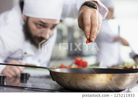 Precision and originality shine as expert adds cut vegetables on a meal on the stove, working in a restaurant kitchen. Professional culinary arts with fresh produce, food prep. 125211933