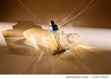 Perfume on a beige background in the rays of bright sun with beautiful highlights. 125213420