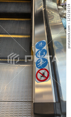 Vertical photo of escalator with sticker icons with rules of use. Safe movement on escalator with observance of rules to prevent injuries during fall on moving staircase 125216154