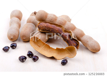 Tamarind fruits, whole, cracked open, and seeds, on a wooden surface. Brown, pod-like fruits of Tamarindus indica, with sweet-sour flavor, typically enjoyed as a paste or candy and used in cuisine. 125216883