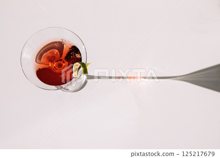 Close-up of a martini glass on a white table. An elegant goblet with a red alcoholic sparkling drink Close-up of a martini glass on a white table. An elegant goblet with a red alcoholic sparkling drink 125217679