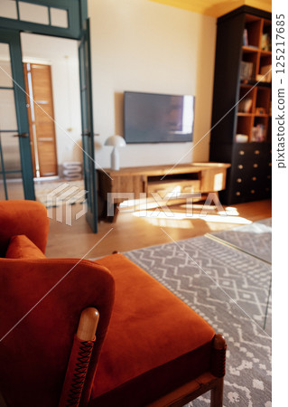 Close-up details of an elegant armchair made of orange fabric and wooden elements. Modern living room with wooden furniture. Bright sunlight. Close-up details of an elegant armchair made of orange fabric and wooden elements. Modern living room with wooden furniture. Bright sunlight. 125217685