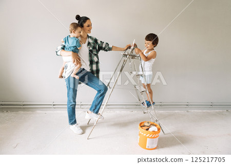 A small boy climbs on a ladder in a renovated room. A laughing mother with her sons among construction tools and materials. 125217705