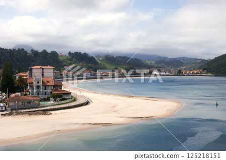 A view of the Ribadesella`s sandy beach, estuary of the river Silla, green hills, mountains, buoy and a promenade along houses with red tiled roofs 125218151