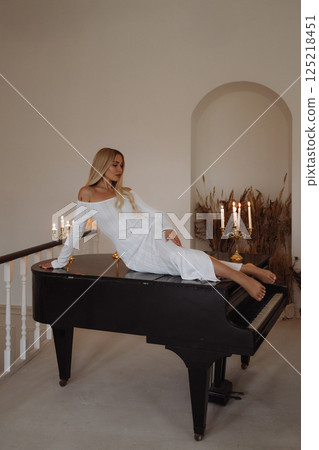 Elegant woman in white dress leaning on black piano. Loft interior. Elegant woman in white dress leaning on black piano. Loft interior. 125218451