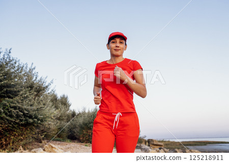 An attractive young woman in a red tracksuit stands on top of a mountain An attractive young woman in a red tracksuit stands on top of a mountain 125218911