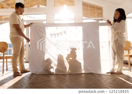 Asian parents play with their children in the living room. Korean mom and dad staged a shadow theater with their kids. 125218935