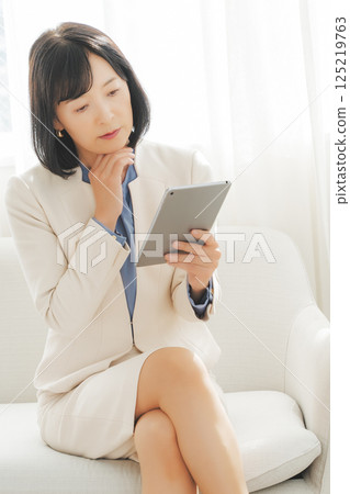 一位中年女性一邊聊天一邊查看平板電腦上的數據 一位中年女性一邊聊天一邊查看平板電腦上的數據 125219763