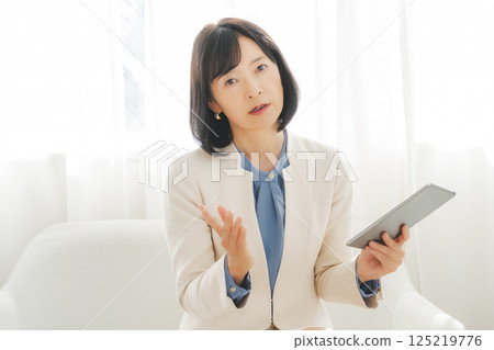 A middle-career woman talking while looking at data on a tablet 125219776