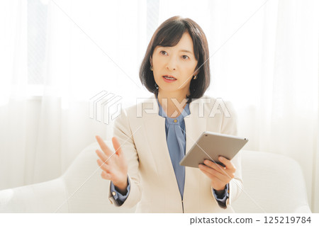 A middle-career woman talking while looking at data on a tablet A middle-career woman talking while looking at data on a tablet 125219784