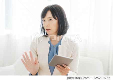 A middle-career woman talking while looking at data on a tablet 125219786