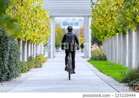 Employee commuting by bike along a green urban pathway, promoting clean transportation Employee commuting by bike along a green urban pathway, promoting clean transportation 125220444
