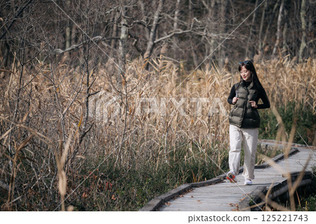 Tranquility in nature, An Asian woman explores a Japanese trail in fall, relishing the solitude and beauty of the journey. 125221743