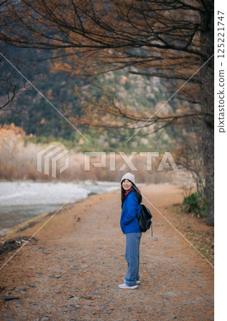 Stylish traveler in Japan, Asian woman in a blue jacket stands by the lake, reflecting on journey of happiness. Elegant portrait capturing the fall mood. 125221747