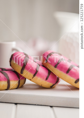 Sweet pink donut with chocolate strips on white table. Sweet pink donut with chocolate strips on white table. 125221759