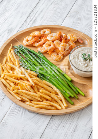Rustic wooden tray serves full meal of shrimp, asparagus, fries, and sauce 125221834
