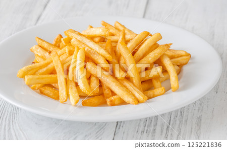 Golden fries piled high on white plate resting on rustic white table 125221836
