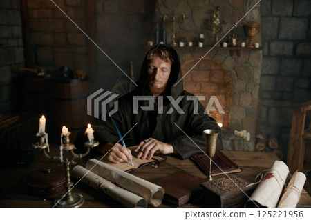Portrait of medieval monk writing historic manuscripts at table 125221956
