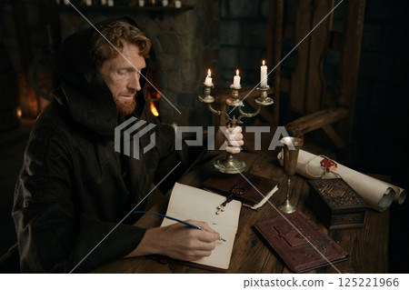 Medieval monk chronicler writing ancient manuscript under candlelight Medieval monk chronicler writing ancient manuscript under candlelight 125221966