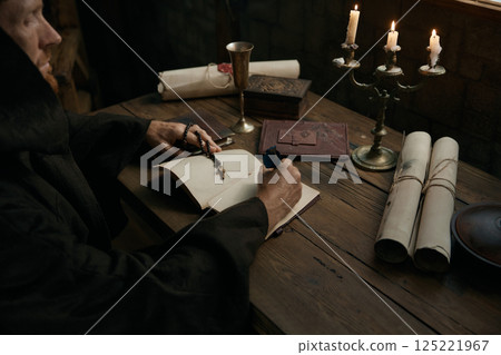 Crop shot of medieval monk chronicler writing ancient manuscript under candlelight 125221967