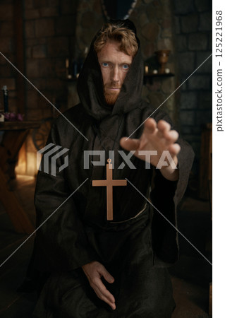 Portrait of friar wearing robe and golden cross reaching hand to camera Portrait of friar wearing robe and golden cross reaching hand to camera 125221968