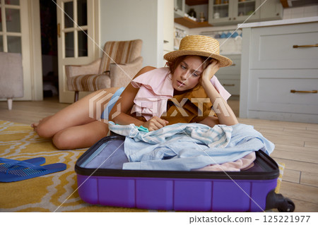 Upset woman tourist looking at excess of travel stuff in opened suitcases 125221977