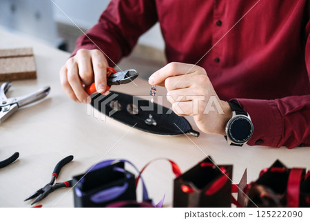 Close-up of artisan hands assembling a custom earring using pliers at a jewelry-making workstation. Custom jewelry, bespoke gifting, emotional commerce, thoughtful design Close-up of artisan hands assembling a custom earring using pliers at a jewelry-making workstation. Custom jewelry, bespoke gifting, emotional commerce, thoughtful design 125222090