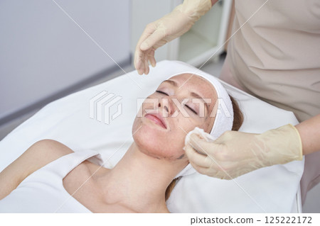 Caucasian female receiving facial treatment in spa setting with gloved hands 125222172