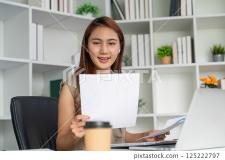 Focused Work and Productivity. A woman reviewing documents while seated at a modern office desk, showcasing her dedication to her tasks. 125222797