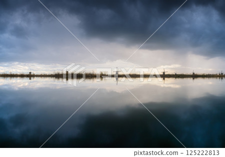 Windmills in the Netherlands during sunset. Storm clouds and sun glow. Dutch canals. Windmills in the Netherlands during sunset. Storm clouds and sun glow. Dutch canals. 125222813