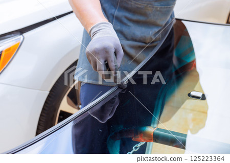 Technician fills applies adhesive car windshield fixes with resin at an auto repair shop 125223364