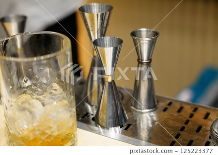 Measuring spirits with stainless steel jiggers at a lively bar countertop 125223377
