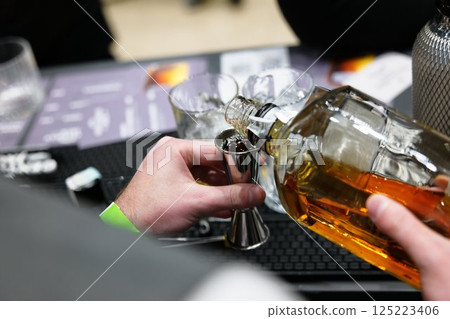 Skillful bartender pours whiskey into a jigger at a trendy cocktail bar 125223406