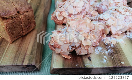 Freshly Baked Almond Croissants and Artisan Bread Presented on Rustic Wooden Boards 125223827