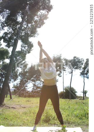 an adult woman doing stretching exercises outside in green park, mental setting training 125223935