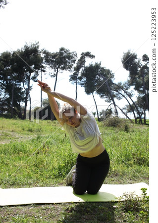an adult woman doing stretching exercises outside in green park, mental setting training 125223953