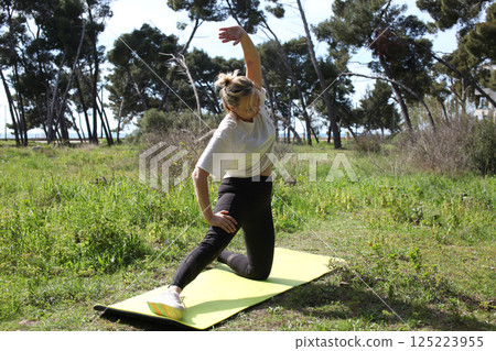 an adult woman doing stretching exercises outside in green park, mental setting training an adult woman doing stretching exercises outside in green park, mental setting training 125223955