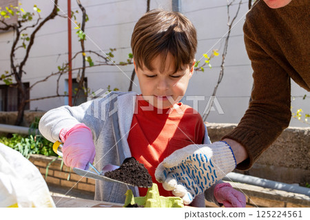 Child pours soil into egg carton for seedlings with parent in backyard garden. 125224561