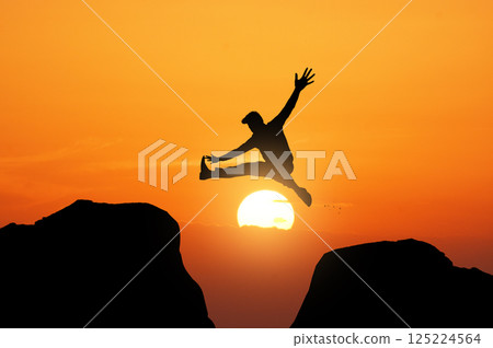 silhouette of a man jumping from one rock to another 125224564