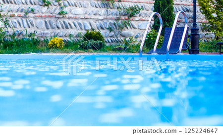 Serene Swimming Pool Surrounded by Lush Greenery and Textured Stone Wall Creating a Relaxing Outdoor Retreat Perfect for Leisure and Summer Fun Serene Swimming Pool Surrounded by Lush Greenery and Textured Stone Wall Creating a Relaxing Outdoor Retreat Perfect for Leisure and Summer Fun 125224647
