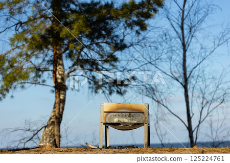 A Tranquil Scene of an Abandoned Grill by the Lake Surrounded by Bare Trees and a Clear Blue Sky, Ideal for Outdoor Activities and Collecting Memories in Nature 125224761