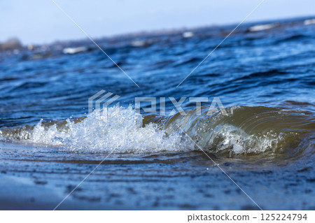 Gentle Wave Crashing on a Sandy Beach Under Clear Blue Sky, Showcasing the Beauty and Serentiy of Nature's Oceanic Environment for Relaxation and Rejuvenation 125224794