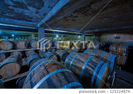 A Dimly Lit Wine Cellar Filled with Numerous Wooden Barrels for Aging Fine Wines in a Rustic Environment Captured in an Atmospheric Interior Scene A Dimly Lit Wine Cellar Filled with Numerous Wooden Barrels for Aging Fine Wines in a Rustic Environment Captured in an Atmospheric Interior Scene 125224874