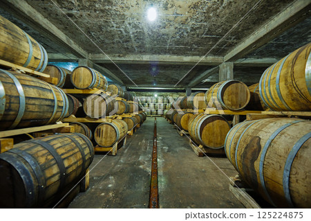 Exploring the Dark Depths of a Rustic Wine Cellar Filled with Wooden Barrels Storing Vintage Wines in the Intimate Ambiance of a Historic Winery. 125224875