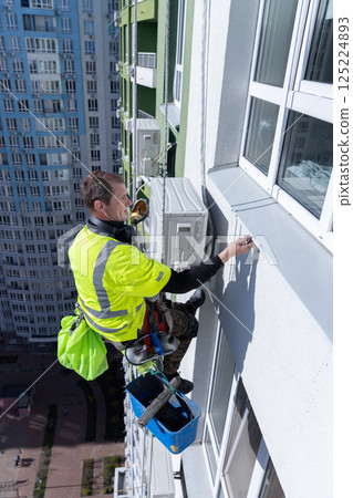 High-Rise Window Cleaner at Work: A Brave Worker Operating on the Edge of Tall Building, Demonstrating Professionalism in Extreme Conditions on a Bright Day 125224893