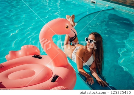 A woman is laying in a pool with a pink inflatable flamingo 125225450