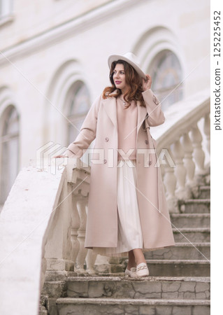 woman in elegant coat and hat against an intricate architectural backdrop, harmoniously blending modern fashion with historical allure. The soft daylight adds to its timeless appeal. woman in elegant coat and hat against an intricate architectural backdrop, harmoniously blending modern fashion with historical allure. The soft daylight adds to its timeless appeal. 125225452