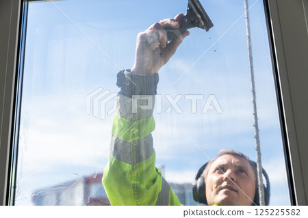 A Dedicated Window Cleaner Hard at Work, Ensuring Crystal Clear Views with Safety Gear, Preparing for a Bright and Clear Day in the Sunshine While Cleaning Glass Windows Professionally 125225582