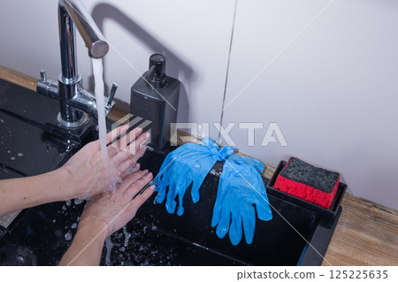 Washing Hands with Focus on Hygiene: A Close-Up View of Hands Under Running Water, Complemented by Blue Gloves and Cleaning Supplies Nearby, Emphasizing the Importance of Cleanliness 125225635